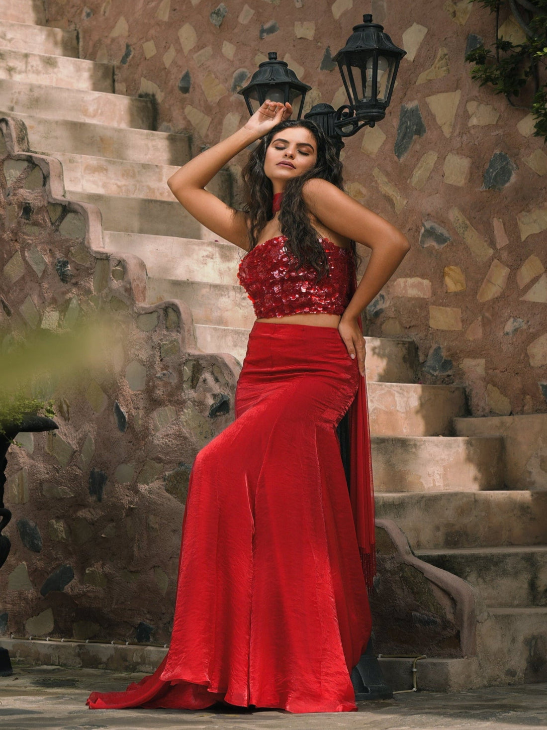 Woman in a red outfit standing on stone steps with a stone wall background